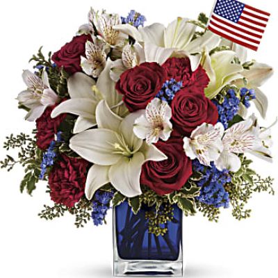 A patriotic pick to send a brave veteran, decorate your Fourth of July picnic, or celebrate Memorial Day. Lush red, white and blue flowers are presented in a glass cube vase along with an American flag.
Red roses, white asiatic lilies, white alstroemeria, blue statice and red carnations are gathered with green pitta negra, seeded eucalyptus and a small American flag in a glass cube.
<ul>
 	<li>Our florists hand-design each arrangement, so colors, varieties and containers may vary due to local availability</li>
</ul>