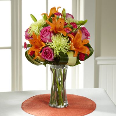 Hot pink bi-colored roses, orange Asiatic Lilies, green Fuji Chrysanthemums, hot pink mini carnations, tropical leaves, and lush greens are brought together to impress, presented in a clear glass vase. Bright, beautiful, and ready to get the party started, this bouquet creates a unique surprise to absolutely delight your recipient with each sunlit bloom.
<ul>
 	<li>Our florists hand-design each arrangement, so colors, varieties and containers may vary due to local availability</li>
</ul>
