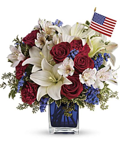 A patriotic pick to send a brave veteran, decorate your Fourth of July picnic, or celebrate Memorial Day. Lush red, white and blue flowers are presented in a glass cube vase along with an American flag.
Red roses, white asiatic lilies, white alstroemeria, blue statice and red carnations are gathered with green pitta negra, seeded eucalyptus and a small American flag in a glass cube.
<ul>
<li>Our florists hand-design each arrangement, so colors, varieties and containers may vary due to local availability</li>
</ul>