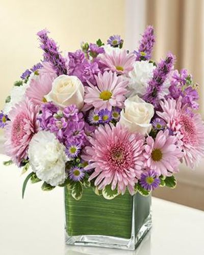 This bouquet features a lavender and white arrangement of roses, stock, liatris, cremones, carnations, daisy poms and monte casino, accented with variegated pittosporum
artistically designed by our florists in a classic clear glass cube vase lined with a Ti leaf ribbon.
<ul>
 	<li>Our florists hand-design each arrangement, so colors, varieties and containers may vary due to local availability</li>
</ul>