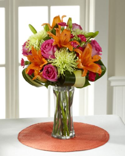 Hot pink bi-colored roses, orange Asiatic Lilies, green Fuji Chrysanthemums, hot pink mini carnations, tropical leaves, and lush greens are brought together to impress, presented in a clear glass vase. Bright, beautiful, and ready to get the party started, this bouquet creates a unique surprise to absolutely delight your recipient with each sunlit bloom.
<ul>
 	<li>Our florists hand-design each arrangement, so colors, varieties and containers may vary due to local availability</li>
</ul>